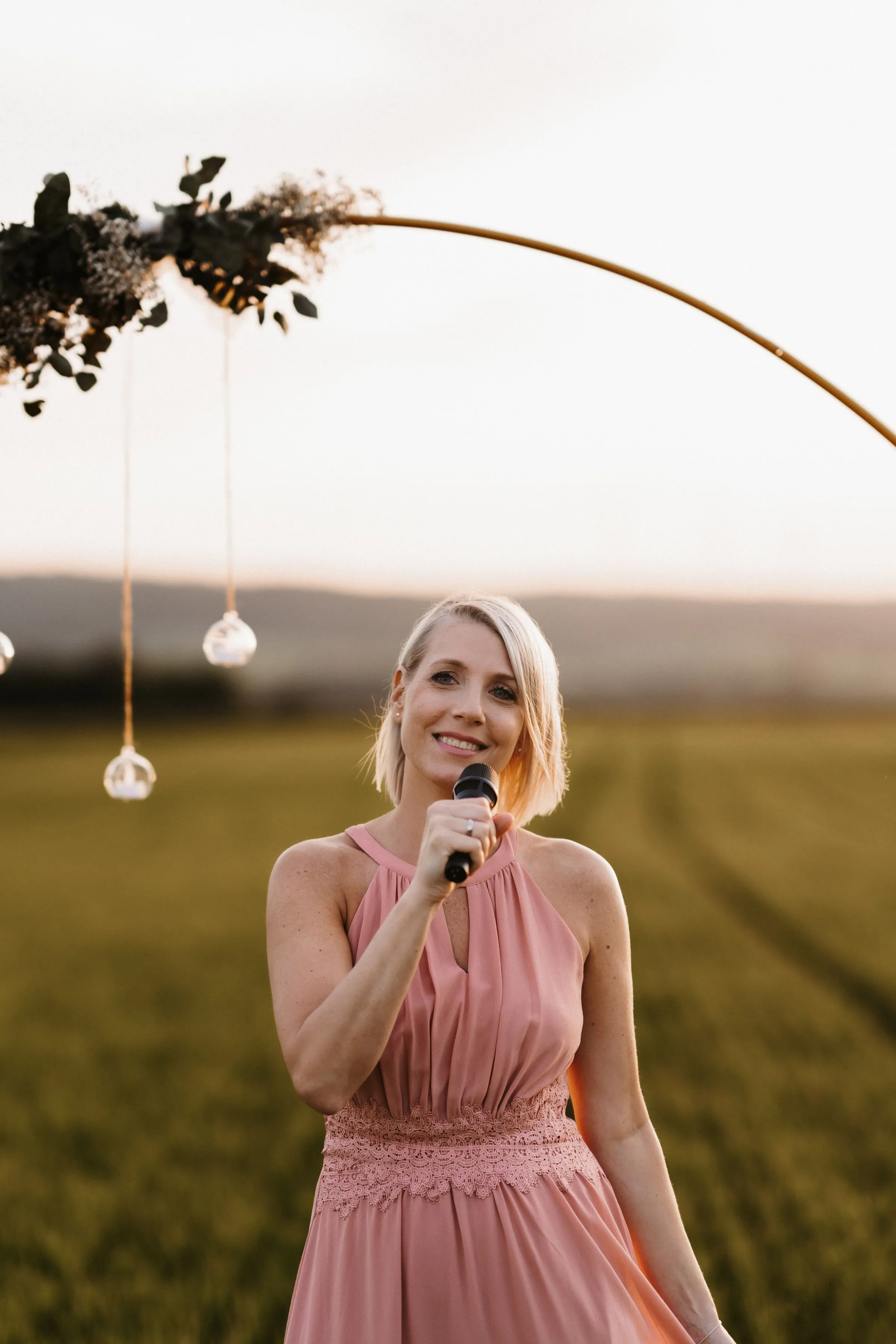 Lisa Dietrich singt mit Mikrofon vor einem goldenen Bogen im Abendlicht