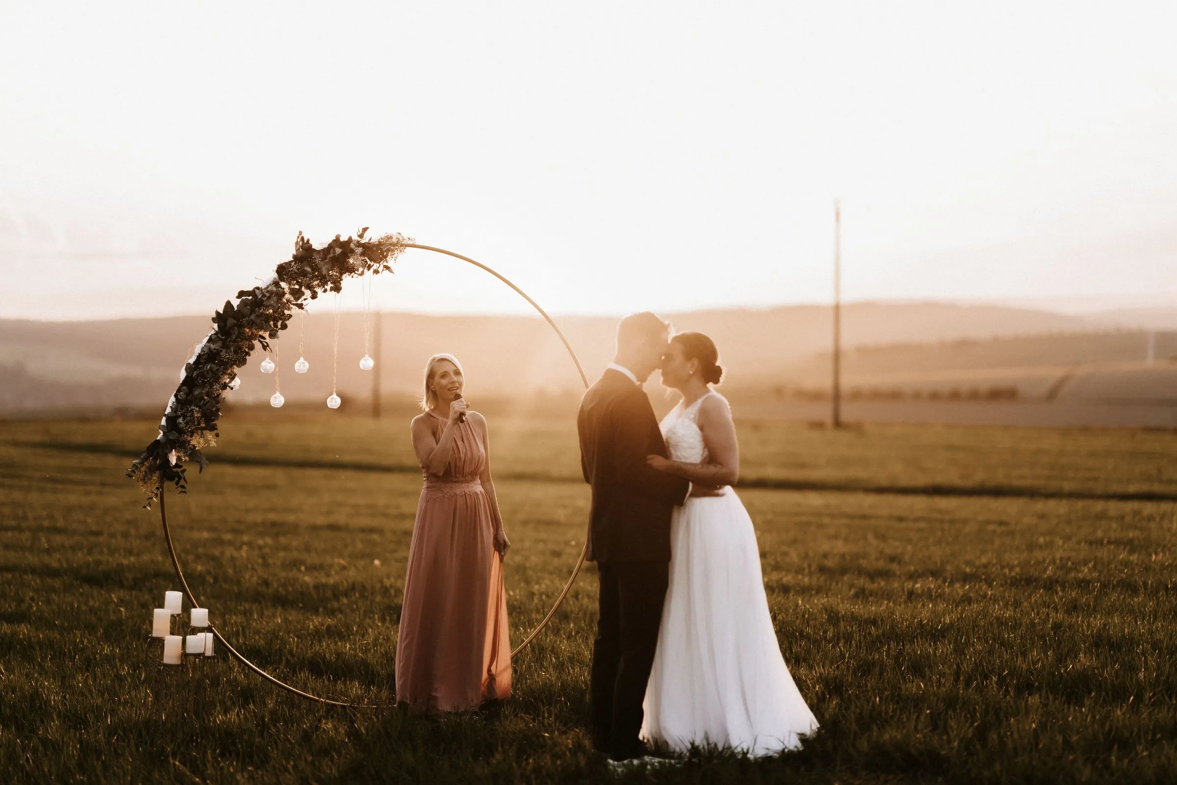 Freie Trauung im Feld mit goldenem Ring und Kerzen im Sonnenuntergang